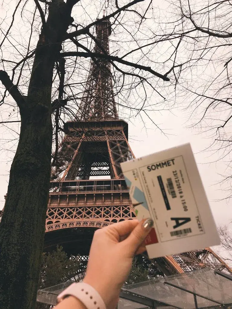hand holding a ticket in front of the Eiffel Tower in Paris